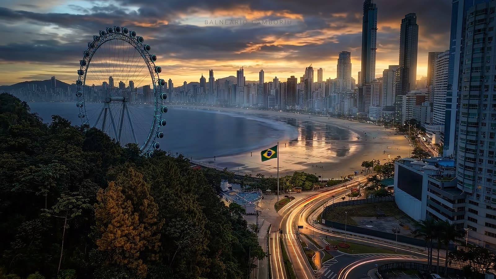 Pôr do sol em Balneário Camboriú (SC) visto do alto: roda-gigante, orla, bandeira do Brasil e os prédios à beira-mar