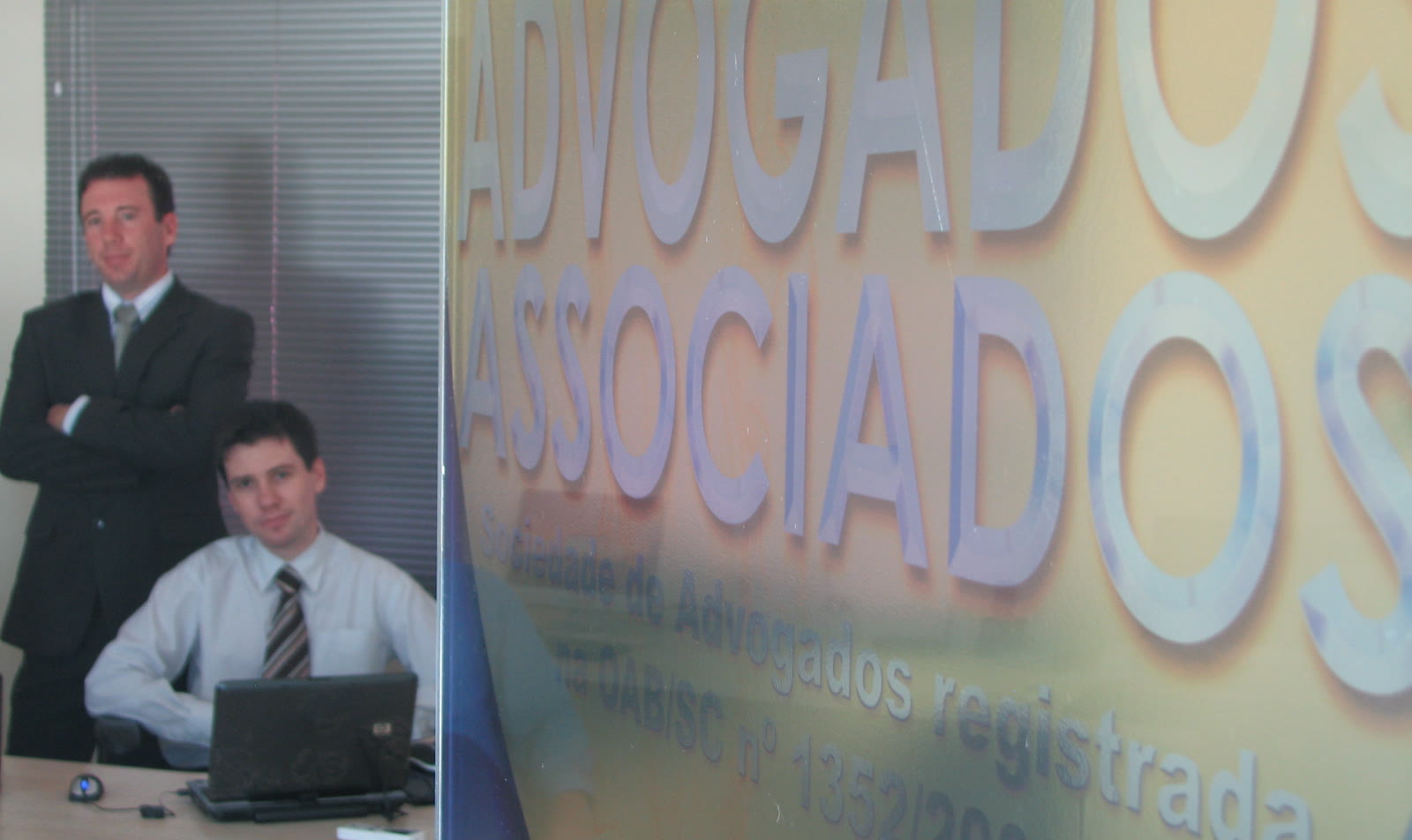 Arquivo dos primeiros anos: Dr. Anderson Macohin, em pé, e André Macohin, sentado ao computador, ao lado da porta com a placa daquela época