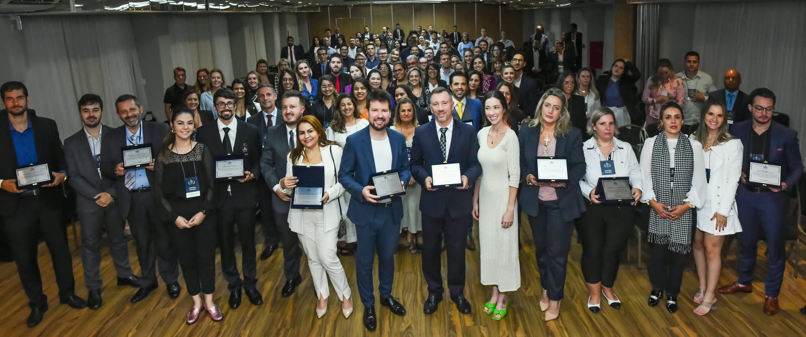 XVIII Simpósio Macohin, em Balneário Camboriú, em abril de 2022: participantes reunidos no salão; à frente, homenageados com placas e, no centro, André Macohin e o Dr. Anderson Macohin.