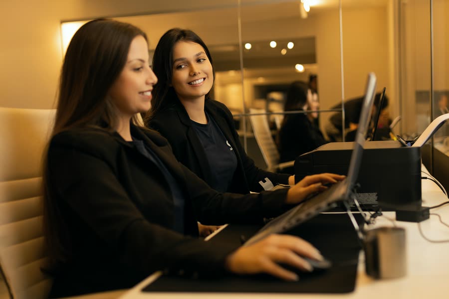 Duas colaboradoras dividem a bancada e conversam enquanto trabalham, em 2025.