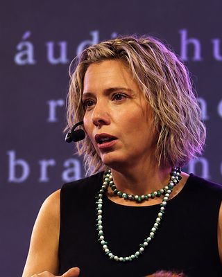 Dra. Alice fala com microfone de cabeça, no palco.