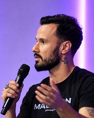 Luís gesticula enquanto fala ao microfone, no painel.