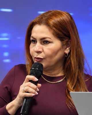 Dra. Mara fala ao microfone, no púlpito.