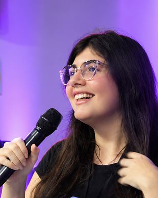 Vero sorri com o microfone na mão, no painel.